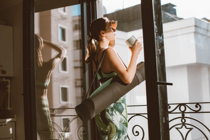 Woman in window with yoga mat and coffee in her hand