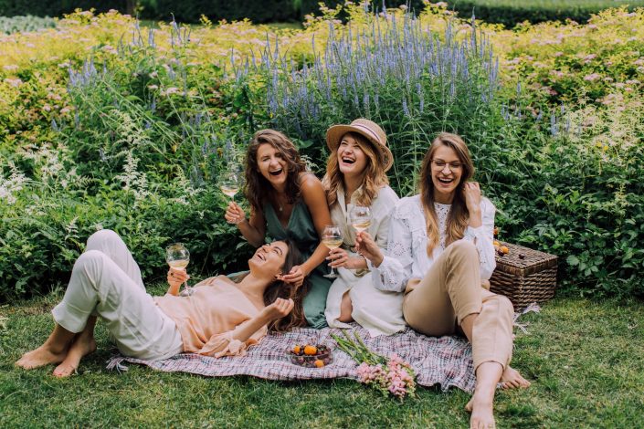 Four women on a picnic blanket in a field of flowers laughing