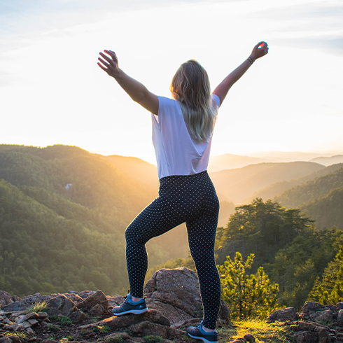 Woman standing with arms out stretched looking at mountain