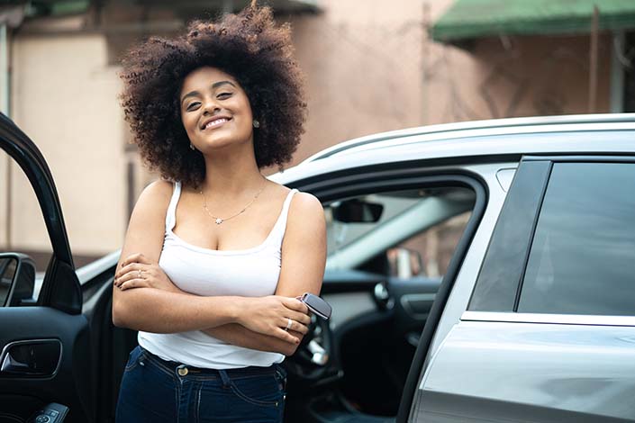 Young Black woman stands near open car door while holding car keys/