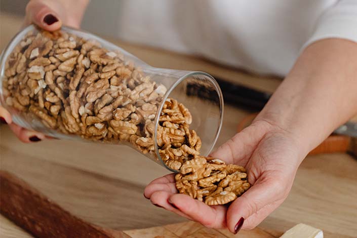 Person pouring walnuts from clear jar into hand