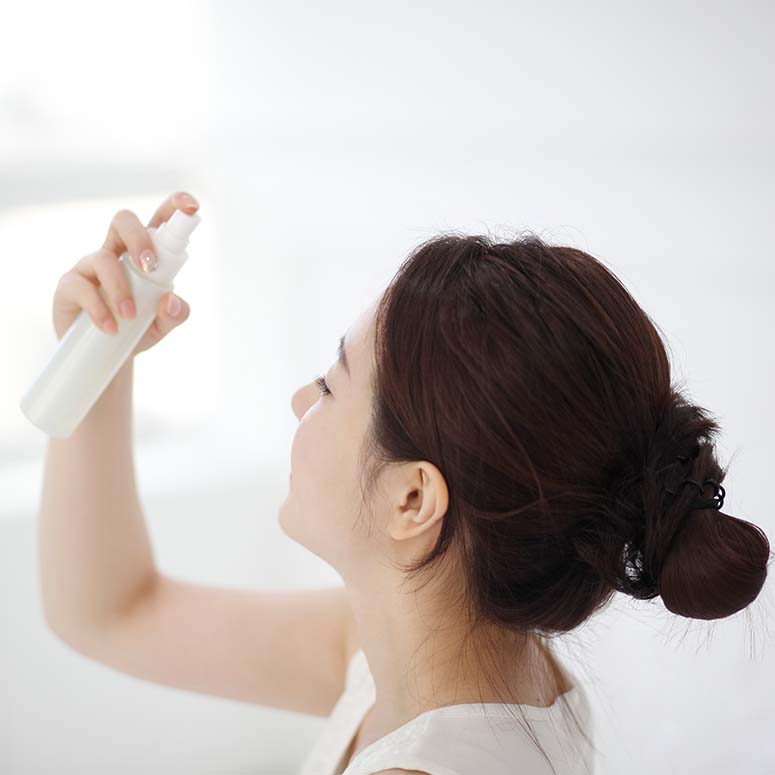 Young woman spraying mist on face