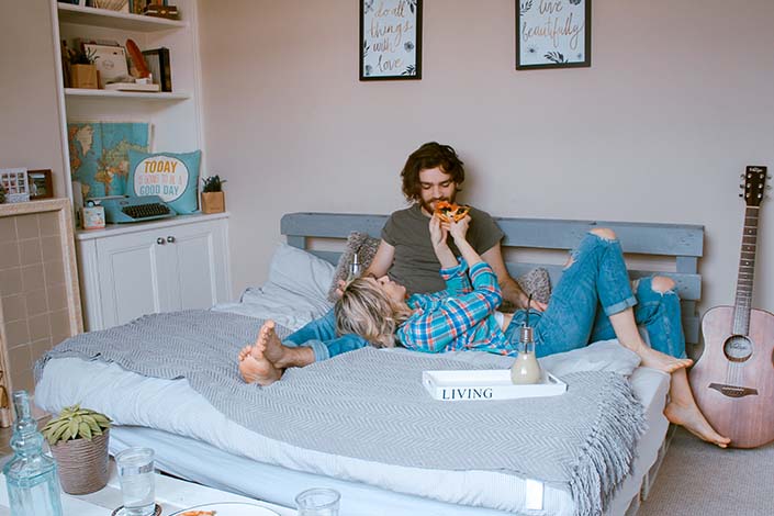 Man and woman eating pizza on a white bed