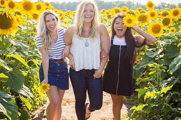Three young women walking in a sunflower field