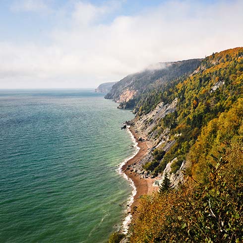 Dissipating fog reveals fall colors and rugged landscape along the Bay of Fundy, Cape Chignecto Provincial Park, Nova Scotia, Canada