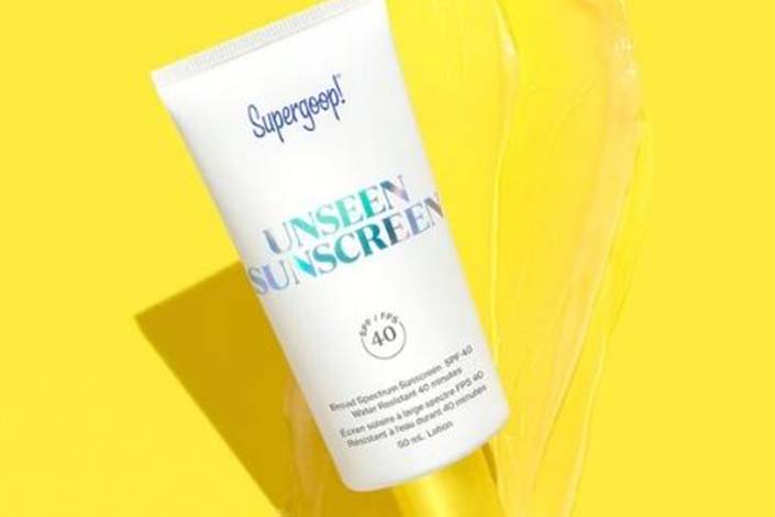 A white and yellow tube of sunscreen on a bright yellow background 