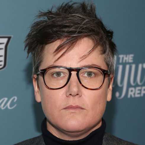 Comedian Hannah Gadsby wearing dark rimmed glasses and looking straight at camera with a serious face.