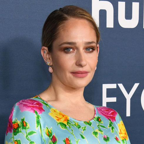 Actress Jemima Kirke wearing a colourful floral dress with her hair tied back, looking at the camera with a small smile.