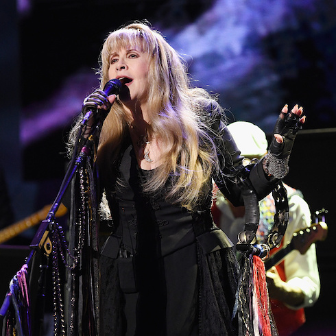 Fleetwood Mac singer Stevie Nicks on stage singing into a microphone with a tambourine on her arm.