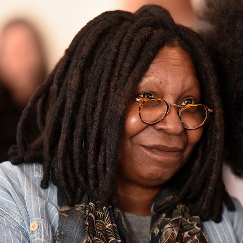 Headshot of Actress Whoopi Goldberg smiling with her mouth closed looking off to the side.