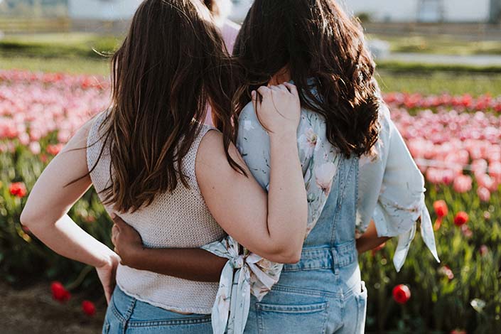Two friends hugging side-by-side in a field of flowers