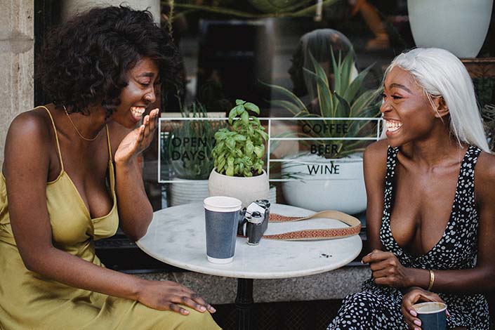Two women laughing while enjoying coffee outside at a cafe