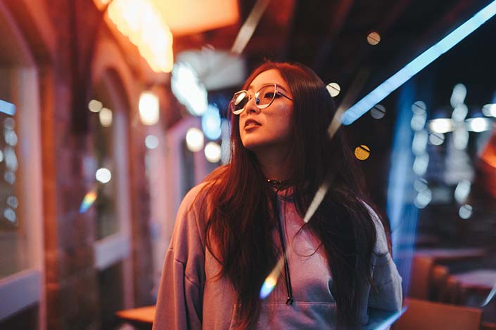 A young woman with glasses walks down the street at night, with lights and neon reflections around her