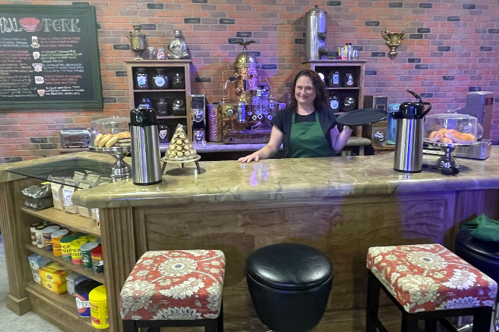 A woman standing behind the counter and holding a tray in a coffee shop with a brick backdrop