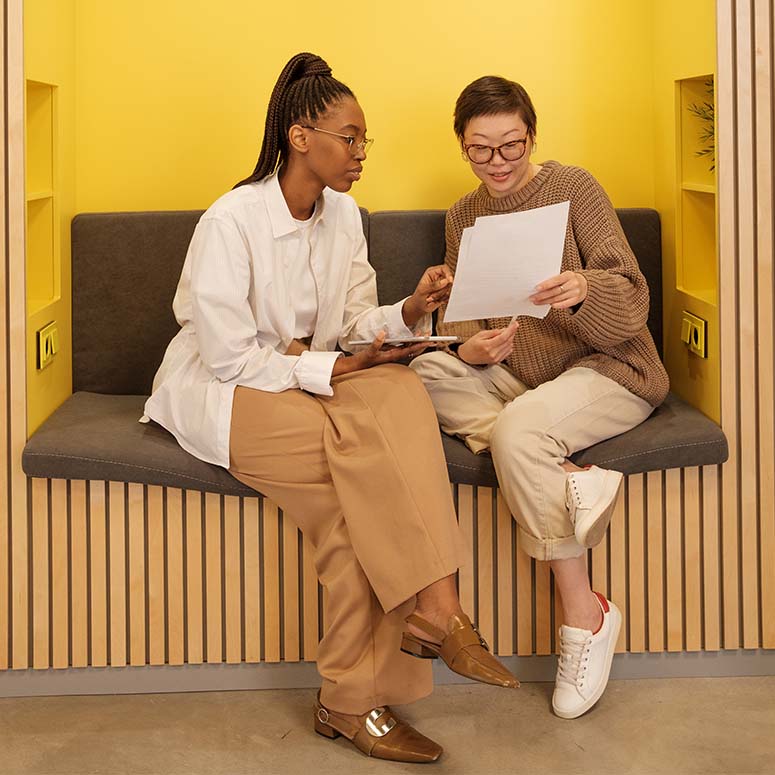 Two women look at a document together while sitting in a yellow booth