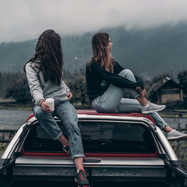 Two women sitting on a car on a cloudy day