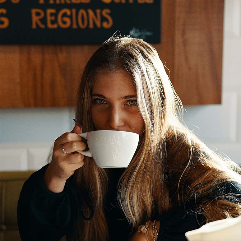 A young woman sips from a white mug