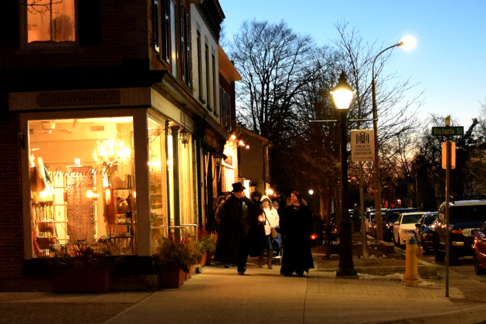 A costumed tour guide takes people on a ghost walk at dusk in Niagara-on-the-Lake