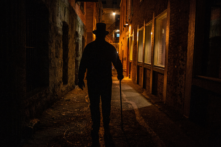 A shadowy figure in Victorian clothes walks down a dark Victoria street