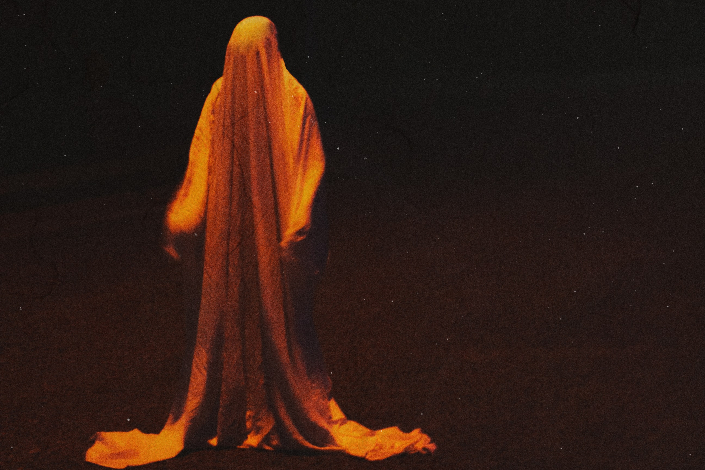 A ghostly figure lit in orange against a black backdrop