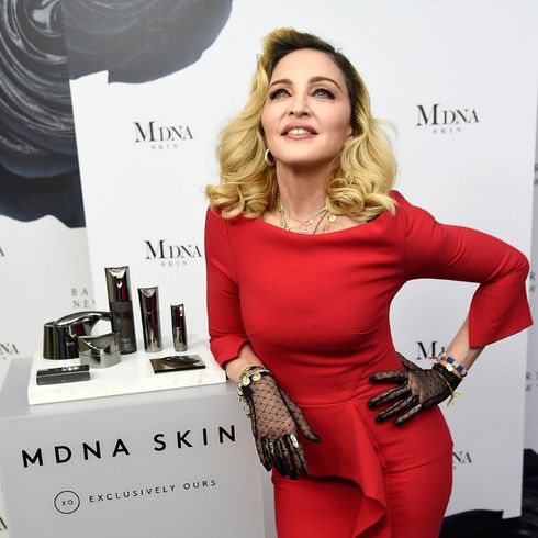Madonna poses in a fitted, long sleeve red dress with black mesh gloves to promote her skincare brand.