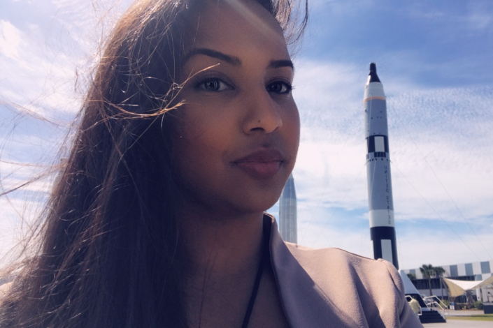 A woman standing outside at Kennedy Space Center with a space rocket in the background