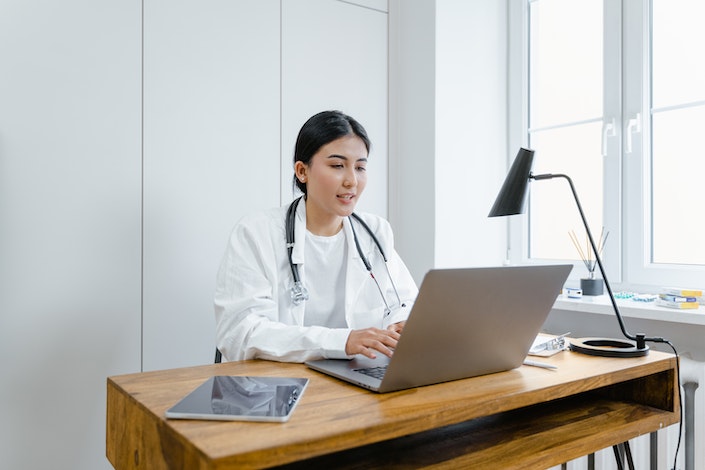 A woman in a white lab coat sits in front of a computer.