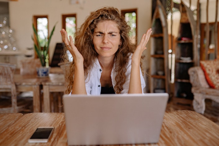 Woman sits at computer with hands thrown up and a frustrated expression.