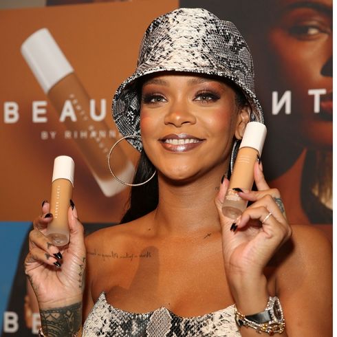 Rihanna smiles for the camera while holding her Fenty Beauty foundation.
