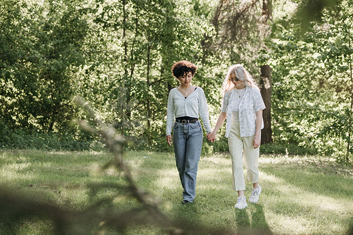 Two women holding hands and walking in a green park
