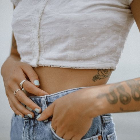 Woman in a white crop top and jeans, holding their stomach