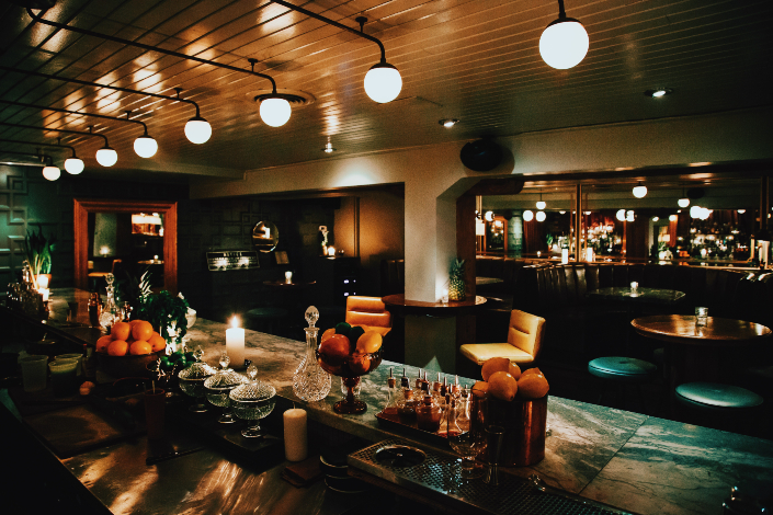 A candlelit bar with beautiful cocktails on the bartop and shelves of bottles