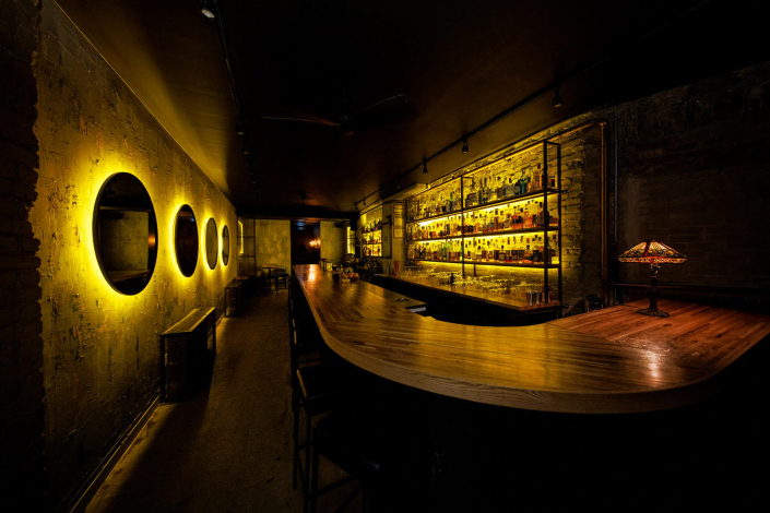 An industrial-style bar with concrete walls and backlit shelving
