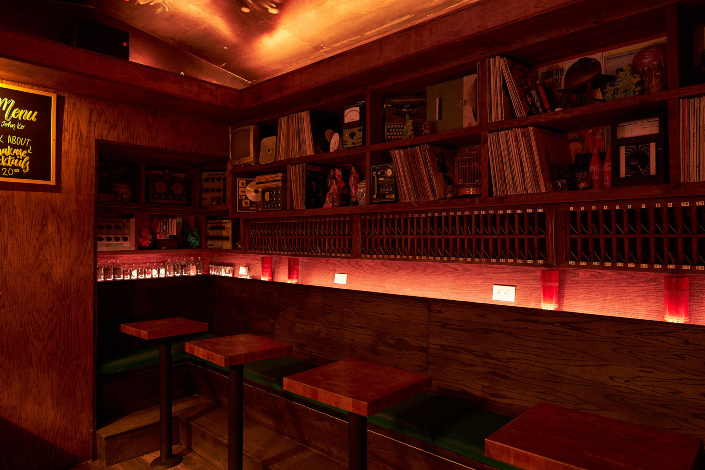 A dimly lit bar with counter seating, stools and built-in shelves on the wall