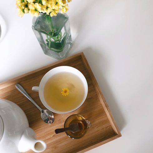 Wooden tray with cup of yellow tea, next to yellow flowers