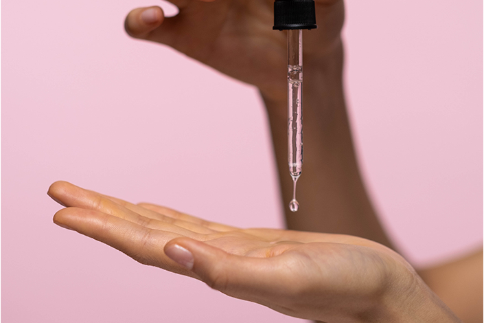 An eyedropper with clear serum drops onto a hand