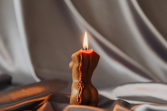 A lit brown candle shaped like a body.