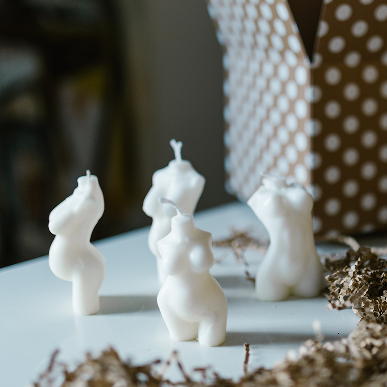 Assorted white candles shaped like bodies beside a polka-dot box.