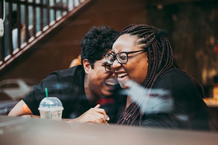 A Black couples laughs happily while sitting at a coffee shop. 