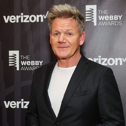 Gordon Ramsay smiles for the camera, wearing a black suit jacket and dress shirt.