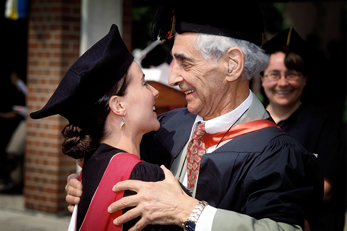 A man and young woman smile at each other and share a hug while wearing graduation clothing.