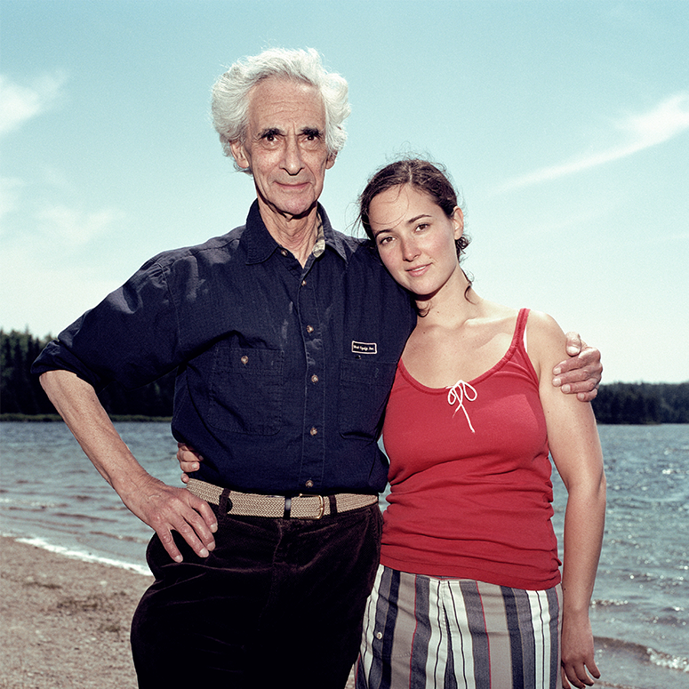 A man with his arm around a young woman, standing at the beach.