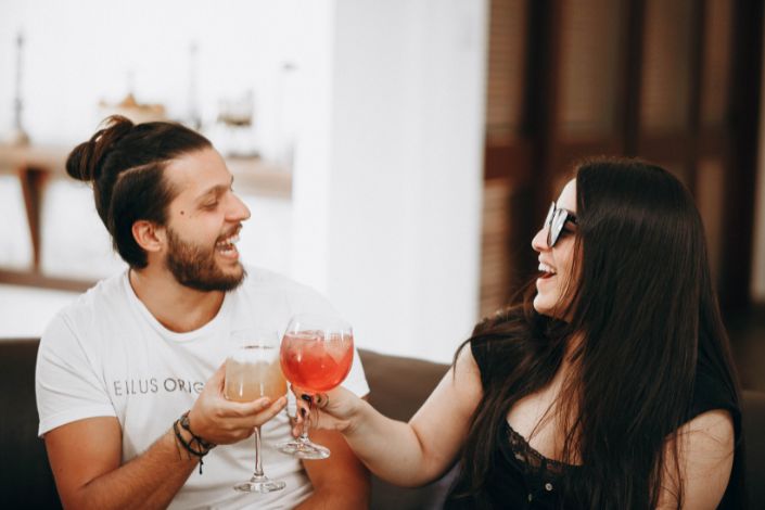 A white man and woman happily enjoy a cheers with different cocktails. 