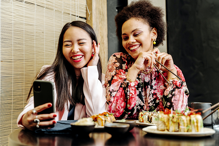 Two smiling women enjoying a sushi meal.
