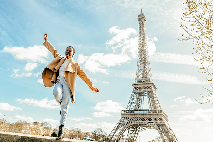 Excited woman jumping from retaining wall with Eiffel Tower in background, Paris