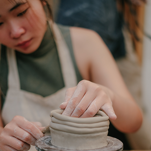 A young woman working on making a clay pot