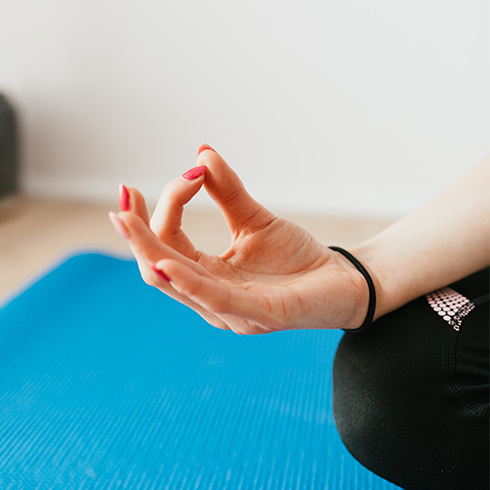 A hand with red nails rests on a person's knee while they meditate.