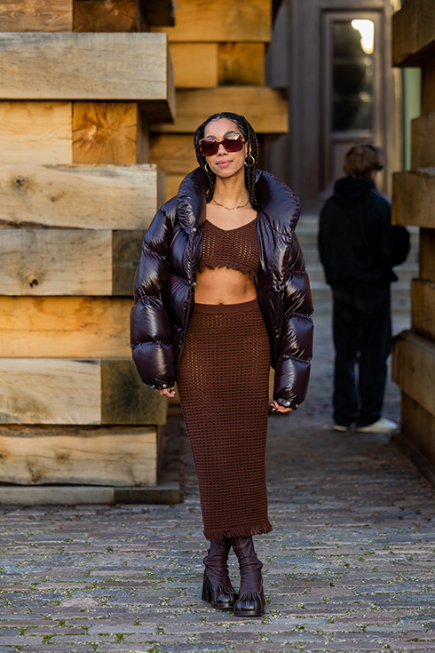 Amaka Hamelijnck wears brown cropped net top, sheer maxi skirt, brown down feather puffer jacket, sunglasses, boots outside Gestuz during the Copenhagen Fashion Week Autumn/Winter 2023 on February 02, 2023 in Copenhagen, Denmark