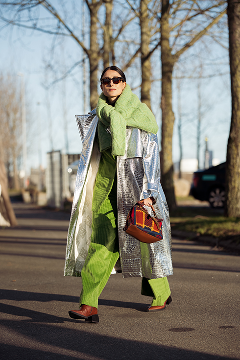 Julia Haghjoo wearing apple green velvet suit, green knitted sweater knotted around the shoulder, long silver coat, brown and red Loewe bag, and brown shoes outside Holzweiler, during the Copenhagen Fashion Week Autumn/Winter 2023 on February 02, 2023 in Copenhagen, Denmark. 