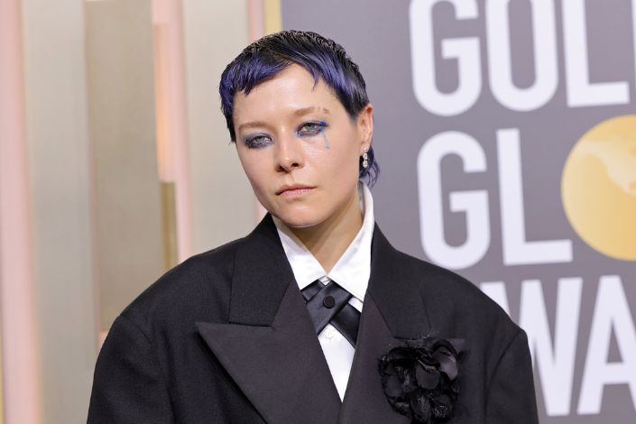 An image of Emma D'Arcy wearing heavy dark eye makeup and a black suit and tie. 
